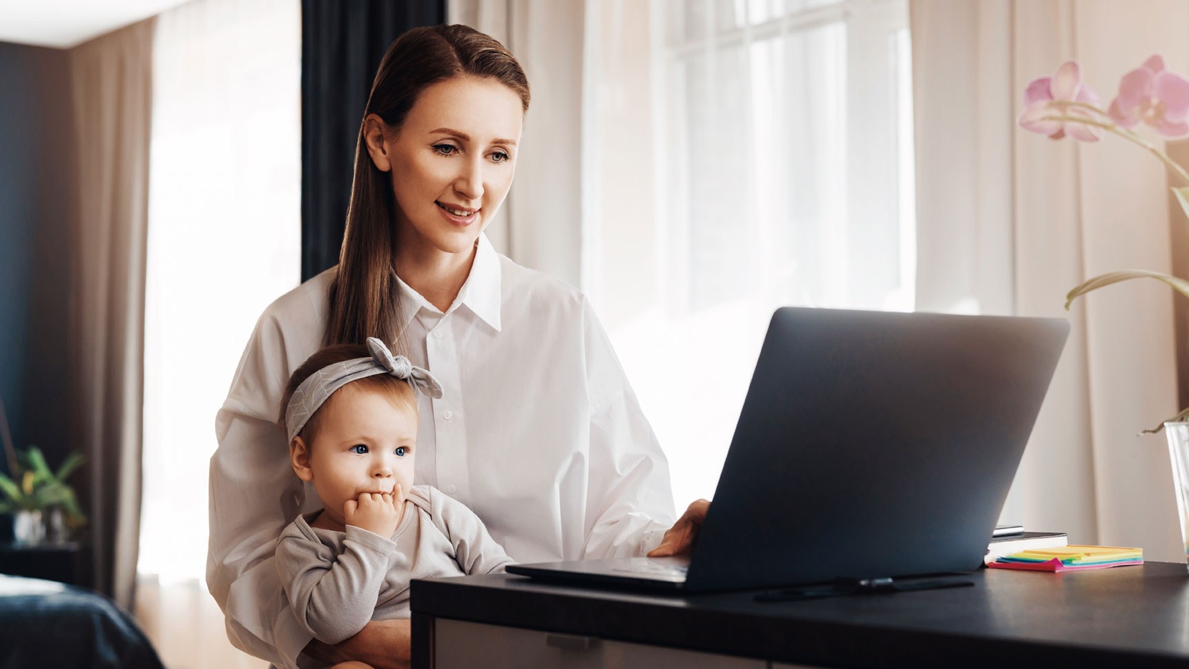 Eine Mutter arbeitet am Laptop. Dabei hat sie ein Kind am Schoß.