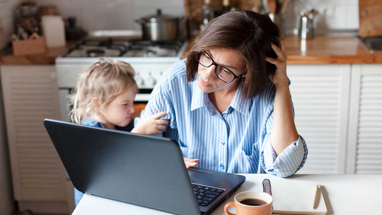 Eine Mutter arbeitet am Laptop, ihr Kind steht neben ihr.