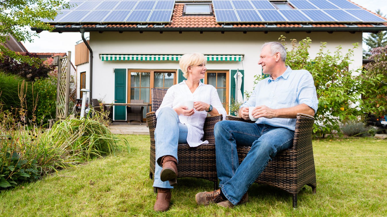 Paar sitzt im Garten vor Ihrem Haus mit Solarpanelen. 