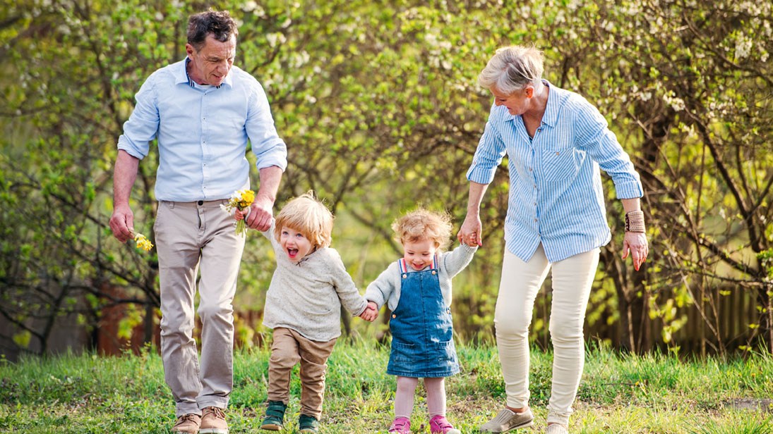 Großeltern gehen mit zwei Enkeln in der Natur spazieren.