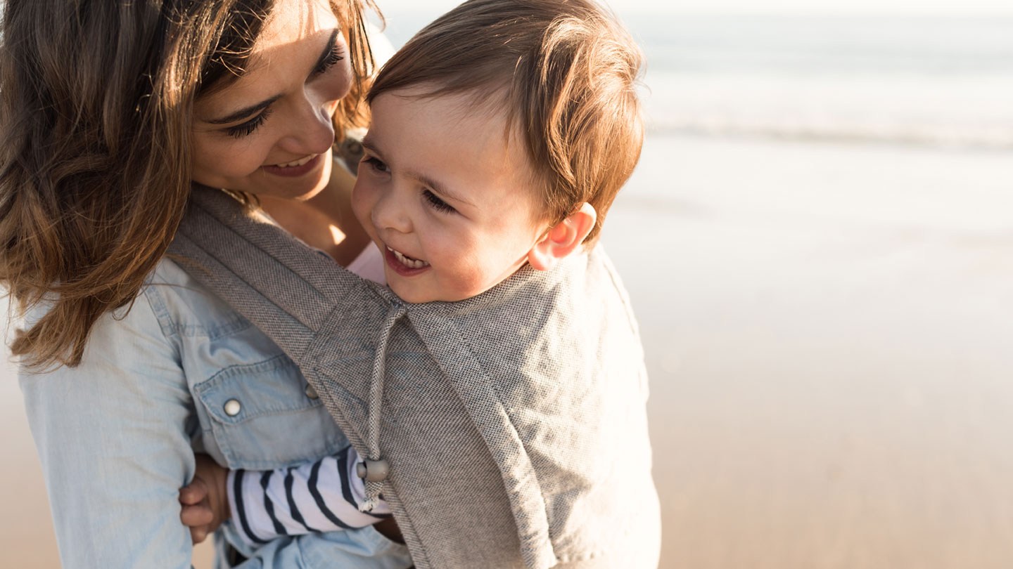 Adoptivmutter trägt Adoptivkind am Strand und lächelt: Eine Adoption rückgängig machen ist in der Regel nicht möglich