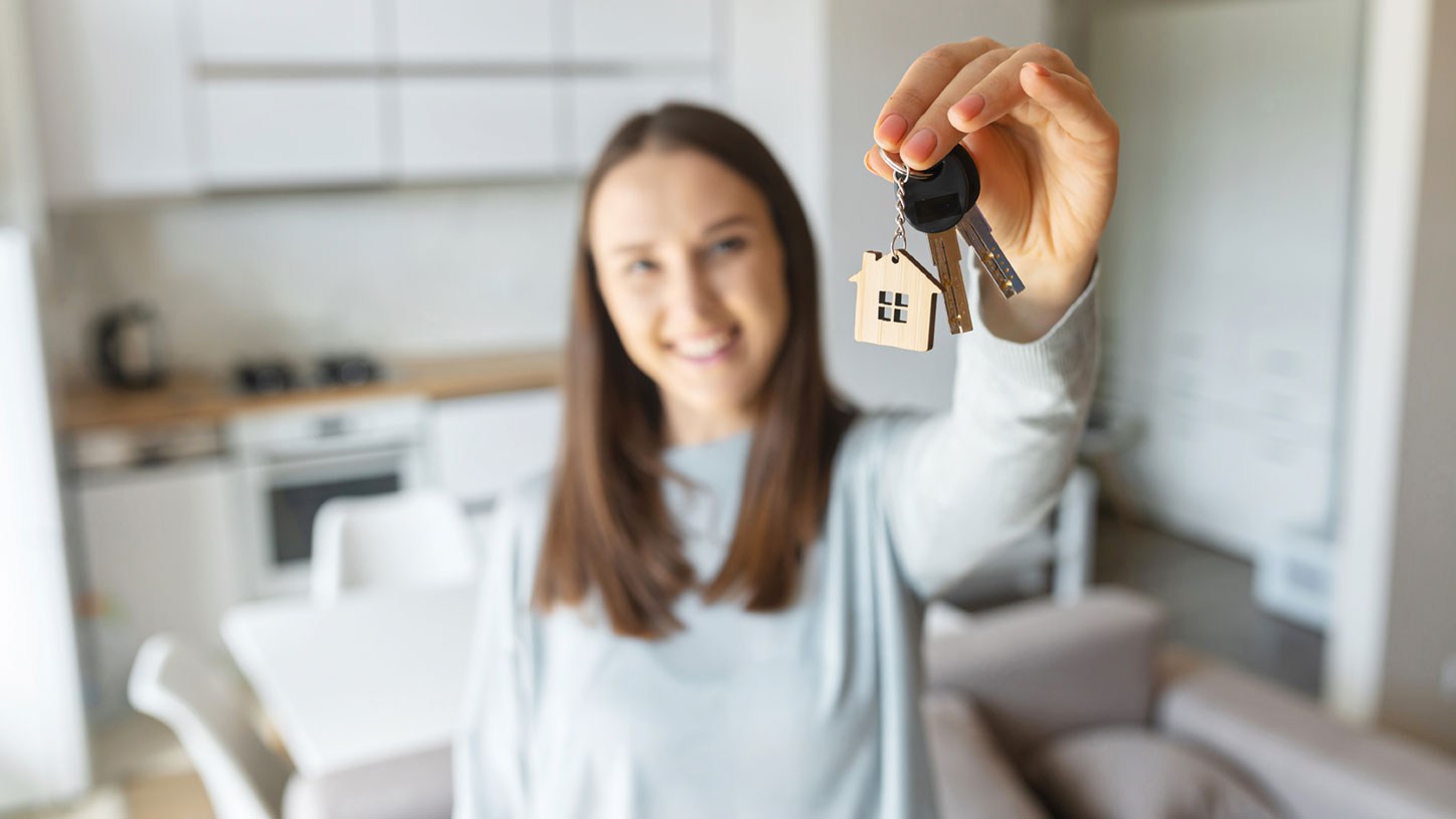 Eine Frau steht in einer Wohnung und hält einen Schlüssel hoch in der Hand