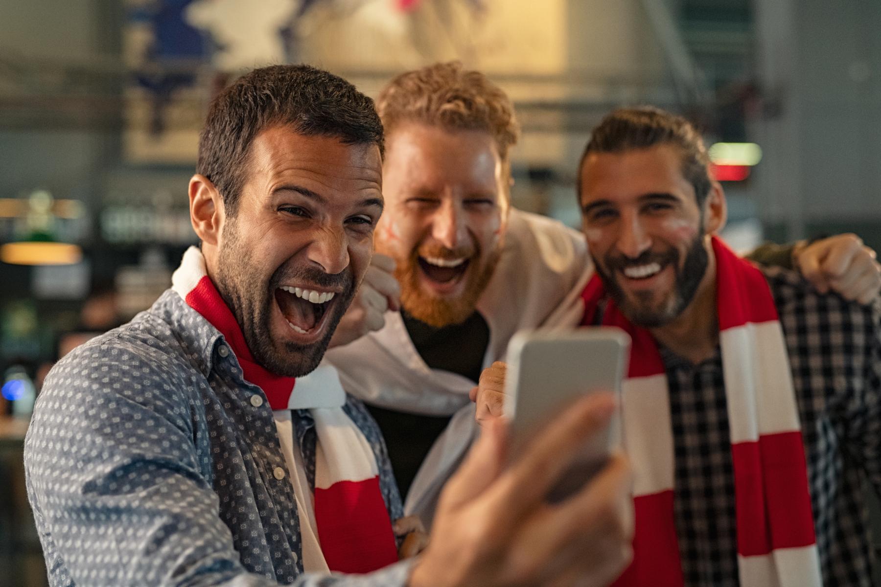 Drei Männer blicken auf das Smartphone und freuen sich das Glücksspiel.