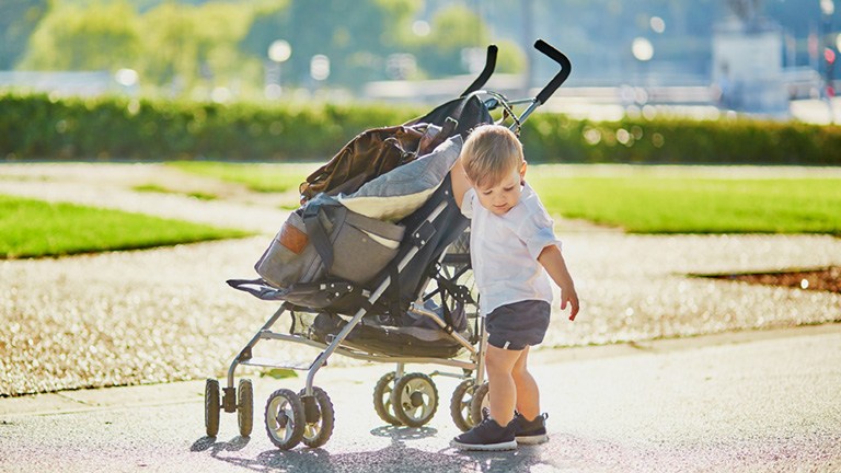 Baby neben Kinderwagen im Park: Seine Mutter hat den Zuschuss für die Baby Erstausstattung beantragt.