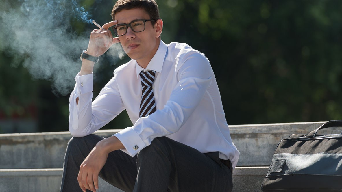 Ein Arbeitnehmer mit Hemd und Krawatte sitzt auf einer Treppe und raucht eine Zigarette.
