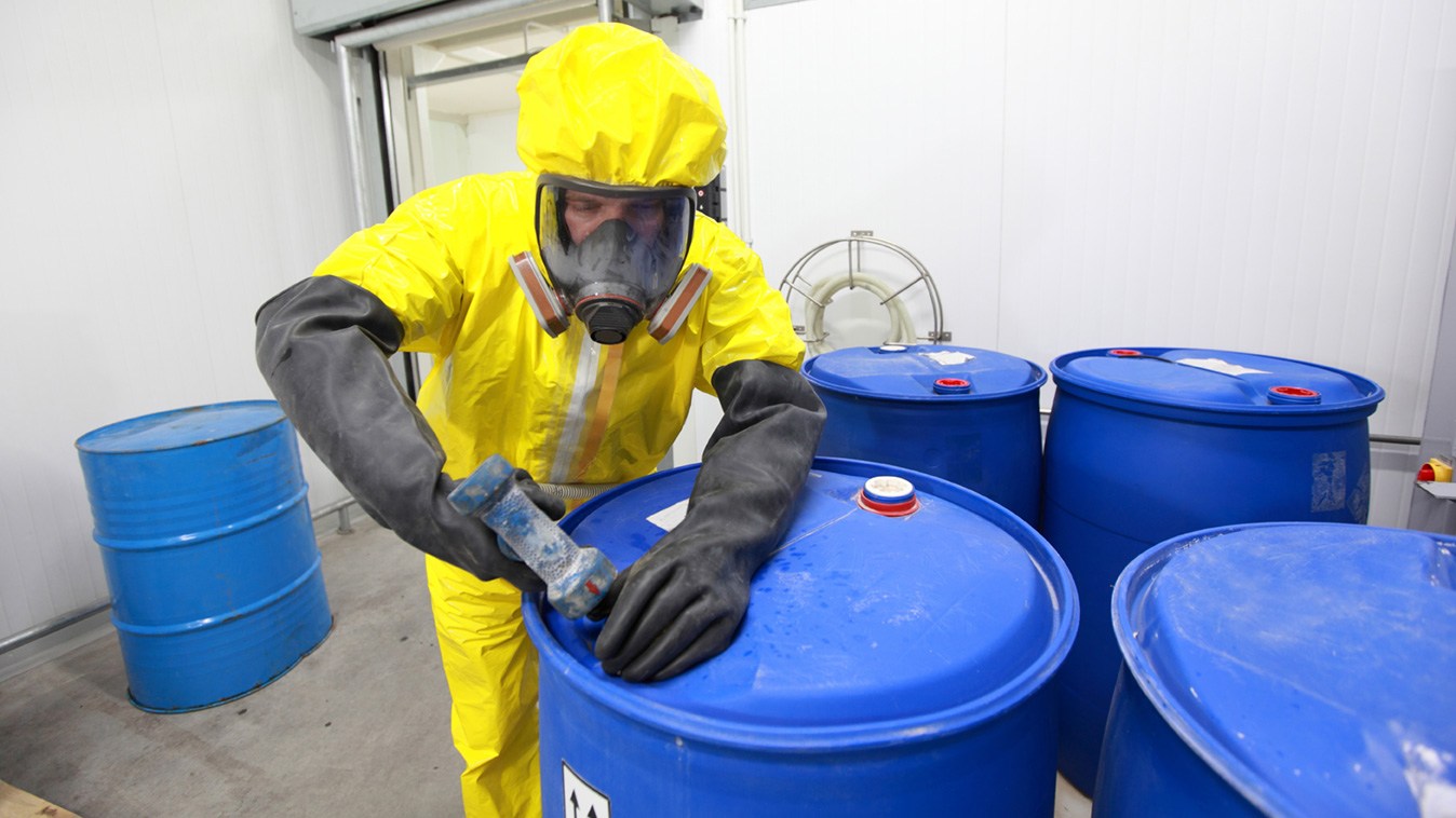Ein Arbeitnehmer in Schutzkleidung hantiert an einem Fass mit Chemikalien.