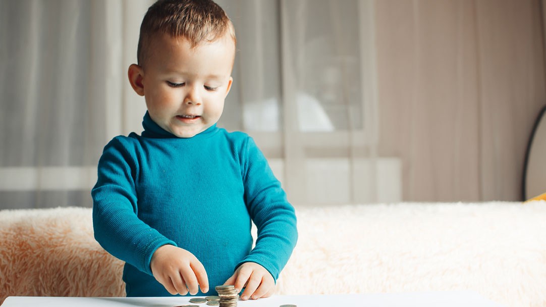 Kleiner Junge spielt mit Geld auf dem Wohnzimmertisch: Seine Mutter fordert Kindesunterhalt rückwirkend.