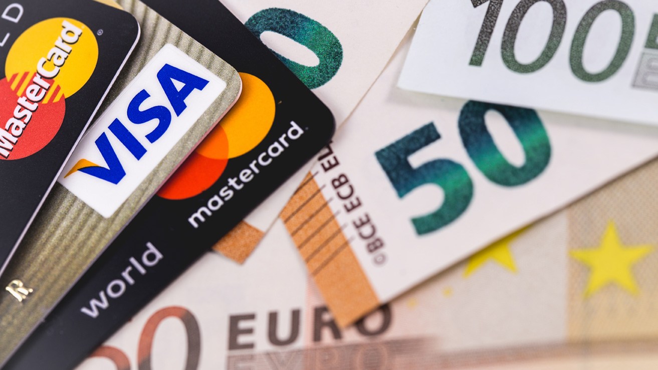 Visa oder Mastercard? Die beliebtesten Kreditkarten und abgehobenes Bargeld liegen auf einem Tisch.