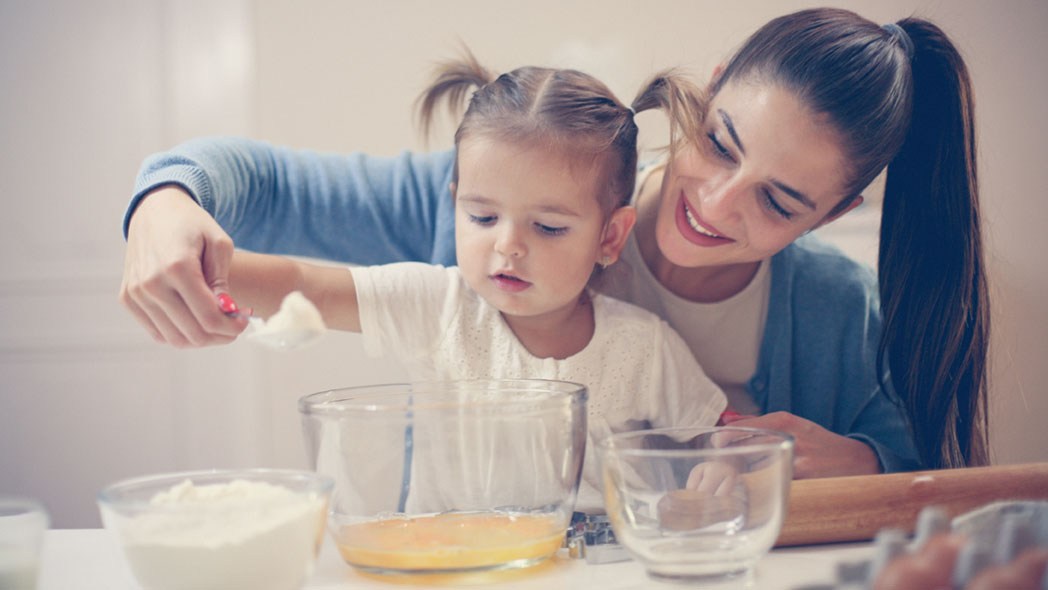 Tagesmutter Kosten: Tagespflegeperson kocht mit Tageskind in der Küche.